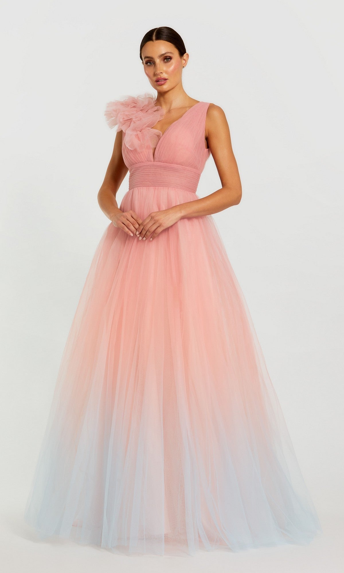 A woman stands against a plain light background wearing the Mac Duggal 37001 long formal dress in Pink Multi—a floor-length, sleeveless tulle ballgown with blue ombre shades and a bold floral accent on one shoulder.